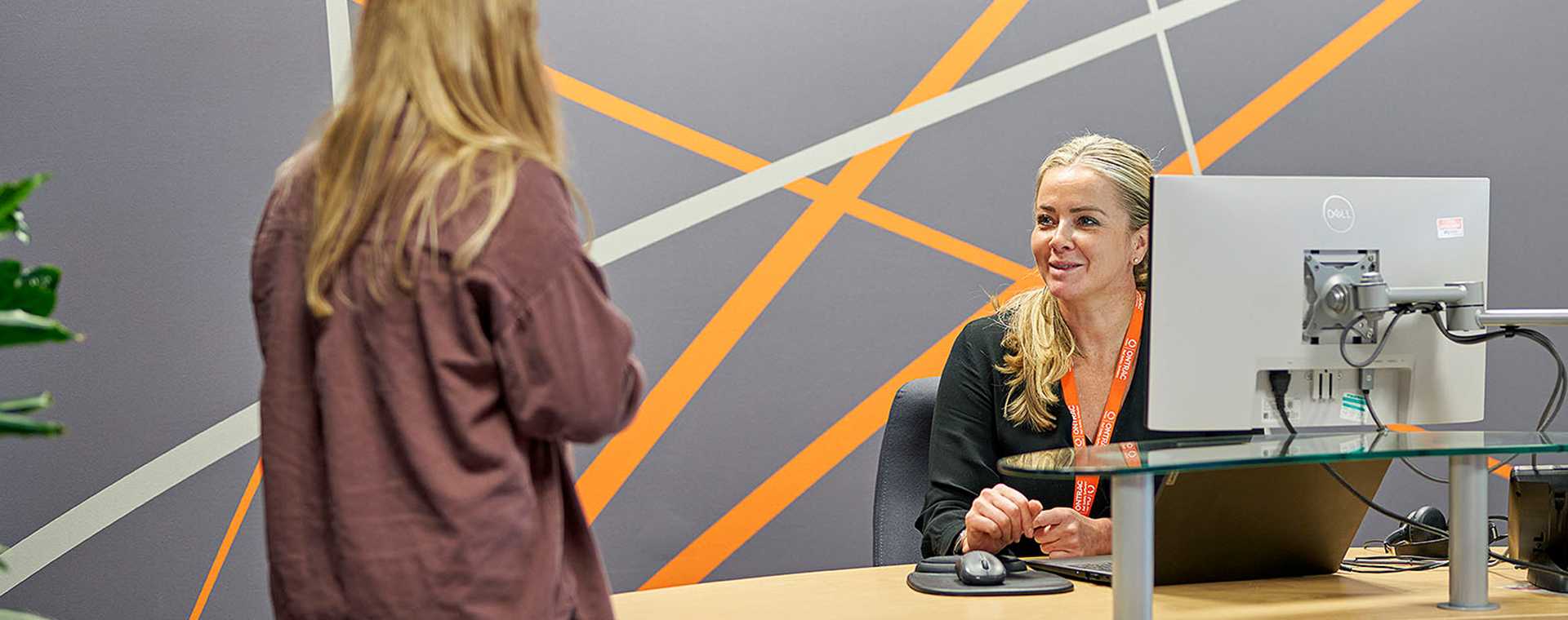 A person behind a desktop computer talking to a colleague